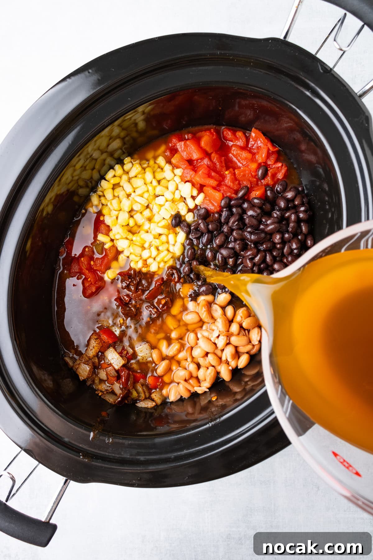 An overhead image of adding vegetable broth and lime juice to the slow cooker.