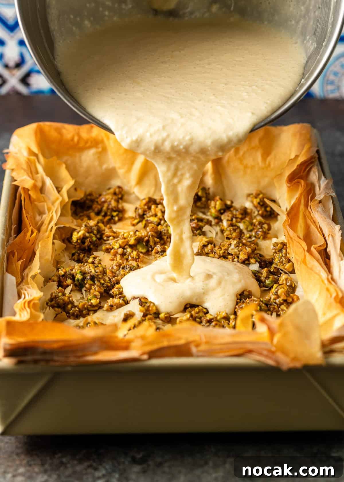 Baklava Cheesecake Bars with Honeyed Pistachios 11 overhead process shot: mixing bowl over top pouring cheesecake mixture into baked baklava