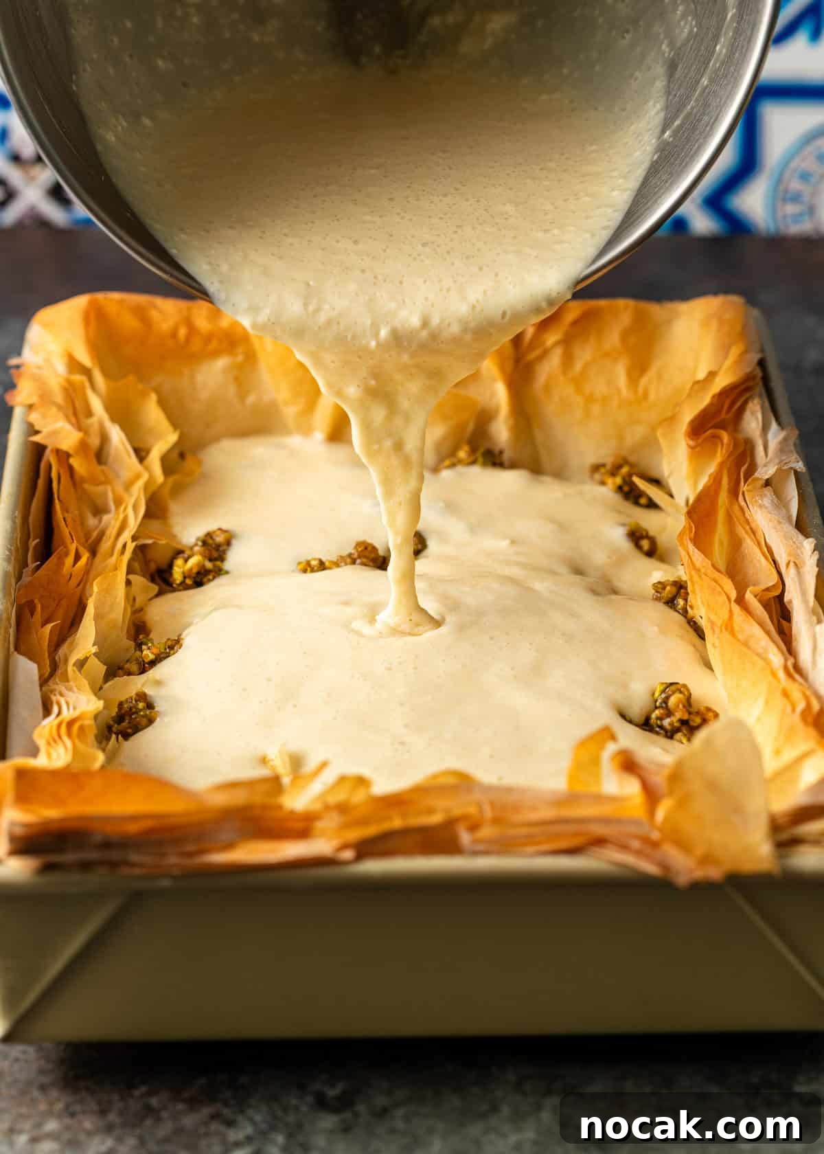 Baklava Cheesecake Bars with Honeyed Pistachios 12 overhead process shot: mixing bowl over top pouring cheesecake mixture into baked baklava