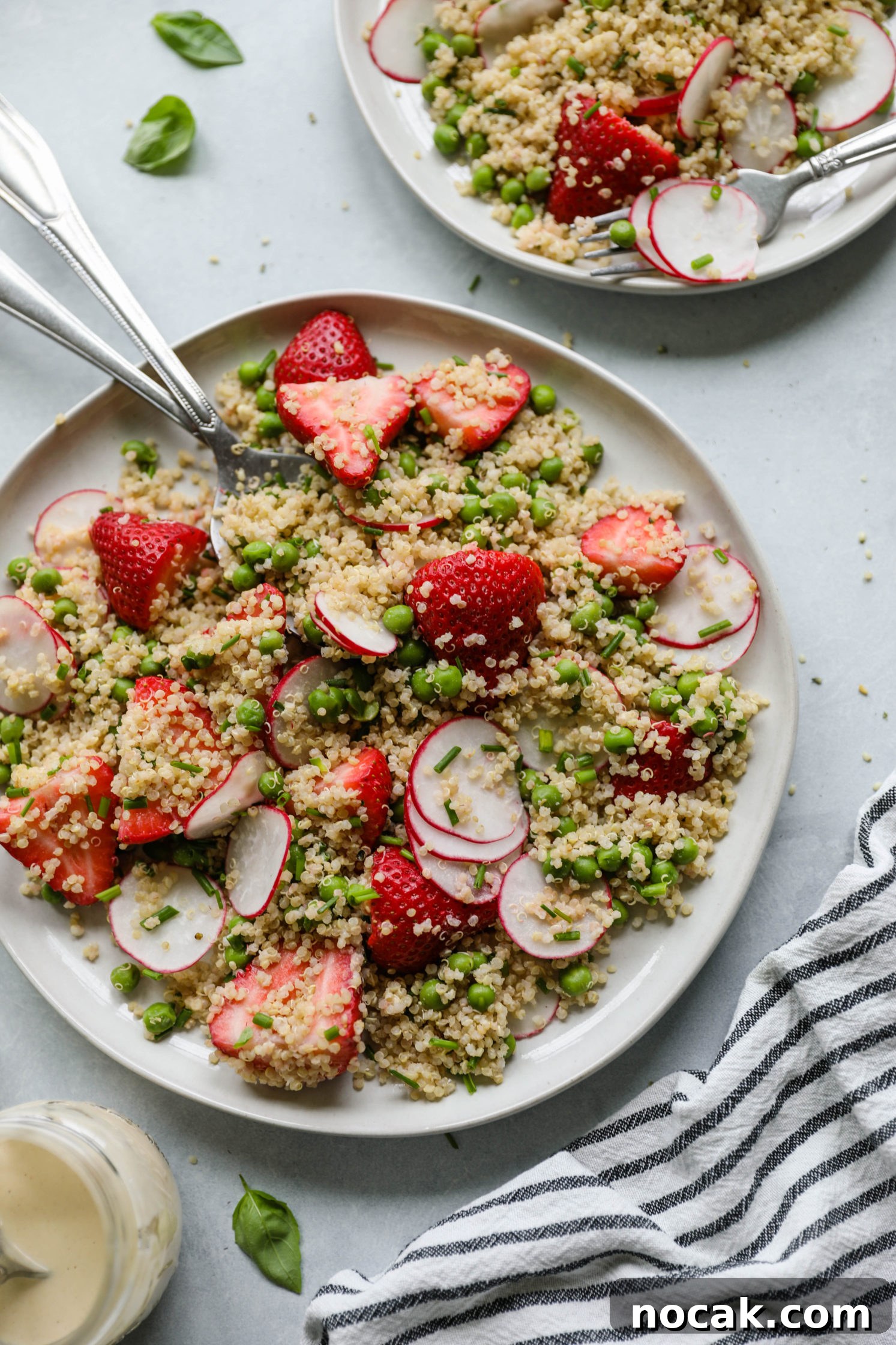 Strawberry Quinoa Salad served on plate with forks with blue and white striped towel with zesty lime tahini dressing