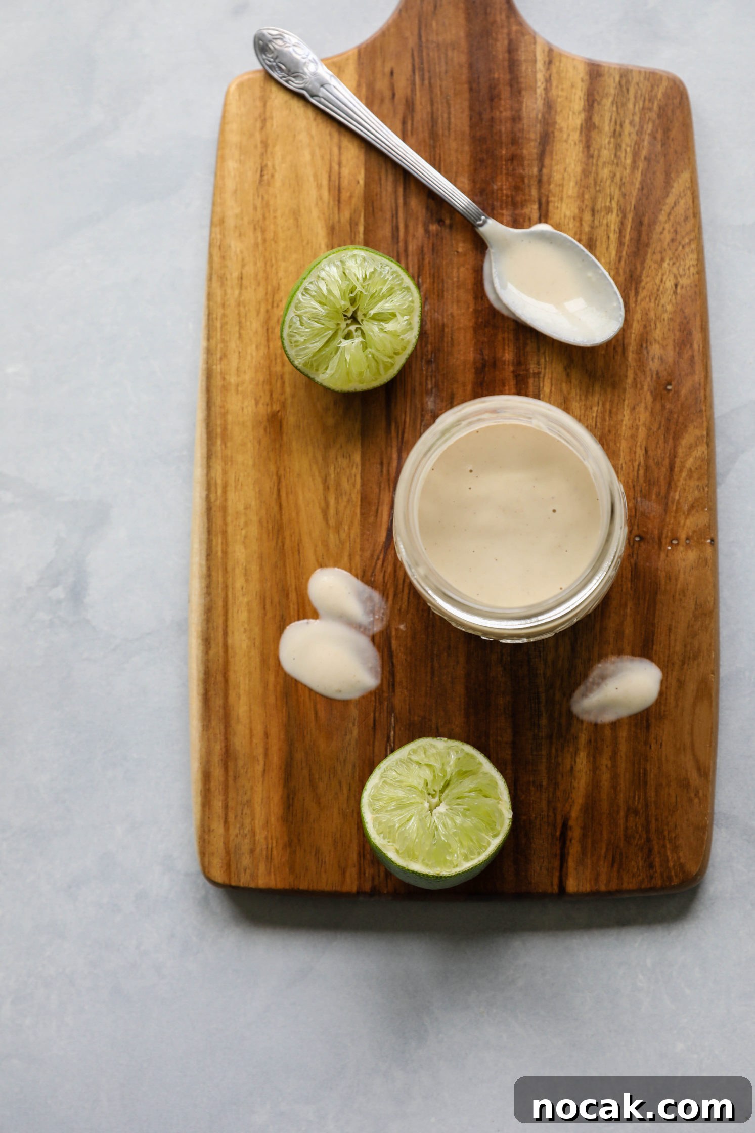 zesty lime tahini dressing mixed in mason jar with spoon and two lime halves on wooden board