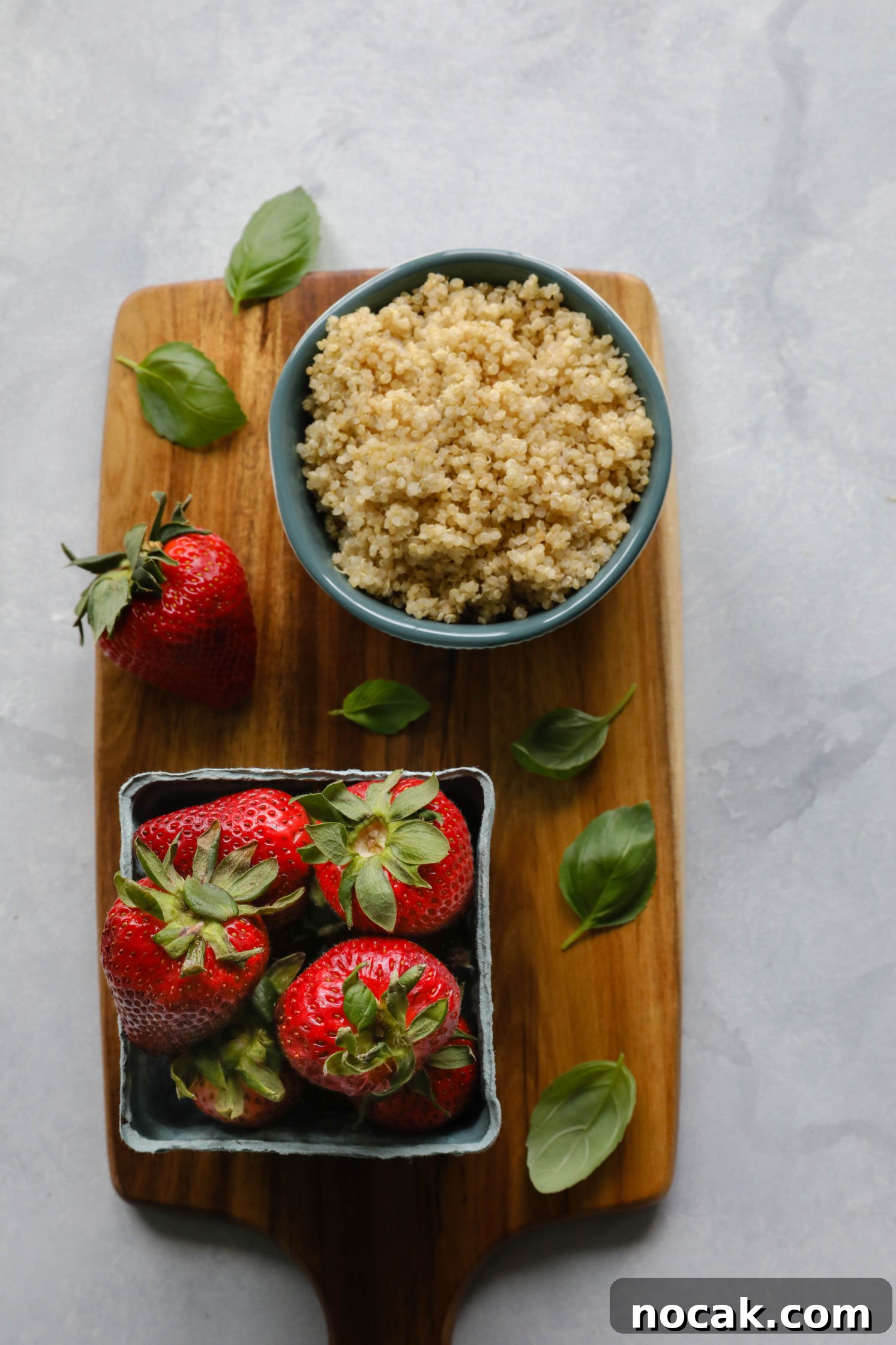 quinoa in bowl with fresh strawberries and basil leaves on wooden board