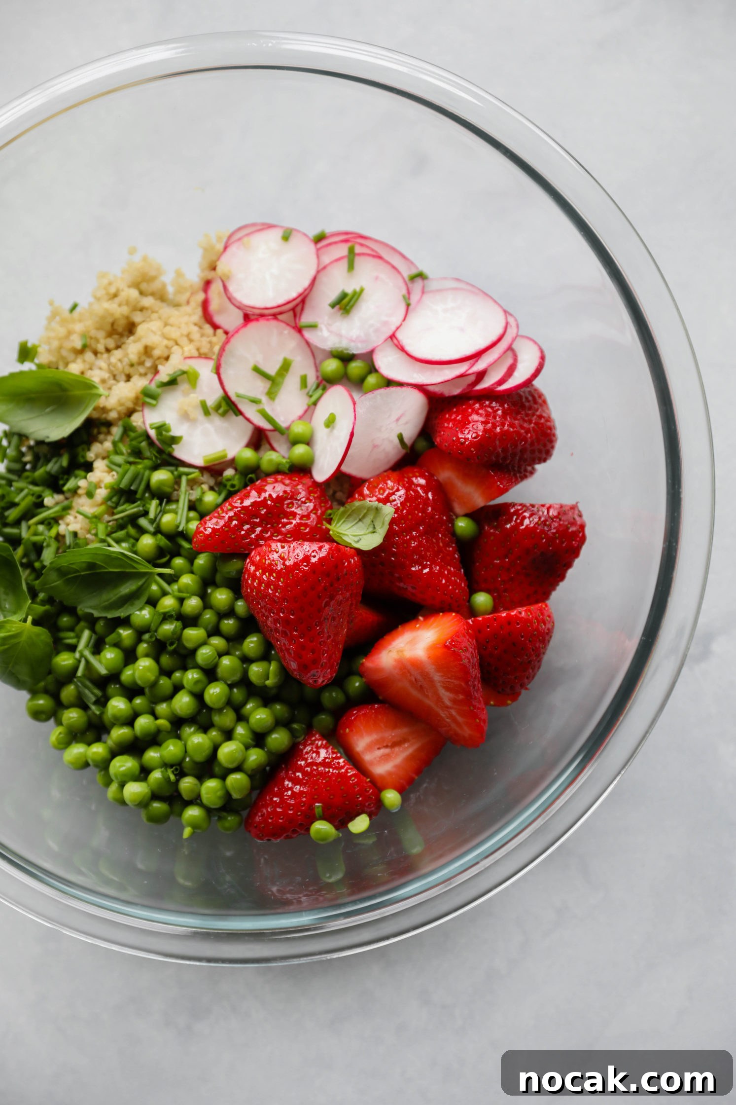quinoa, radishes, strawberries, green peas, basil, and chives in a glass bowl 
