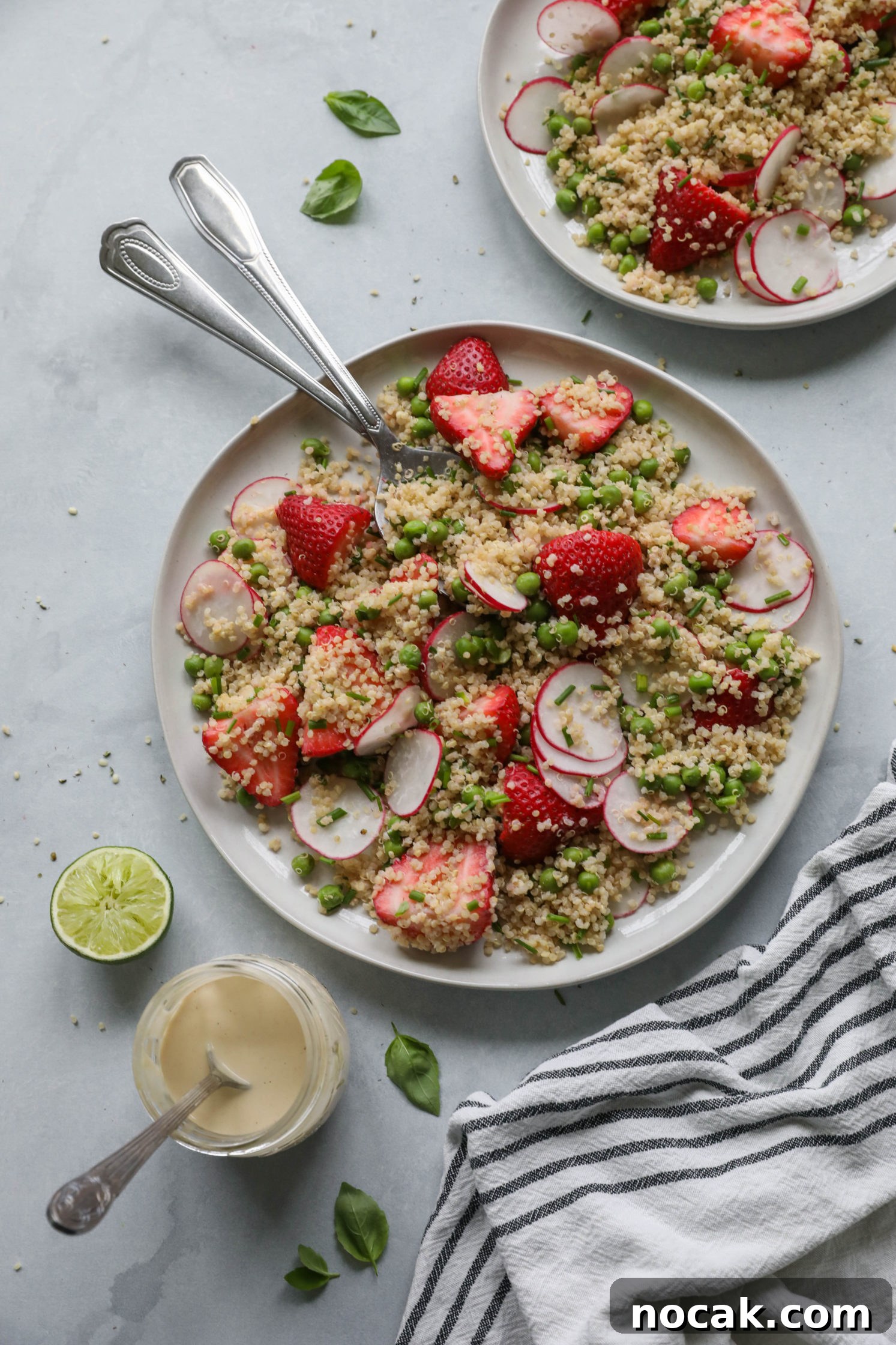 Strawberry Quinoa Salad served on plate with forks with blue and white striped towel with zesty lime tahini dressing