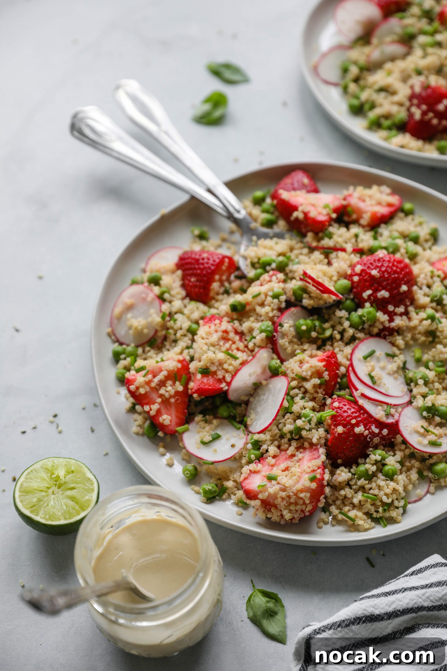 Strawberry Quinoa Salad served on plate with forks with blue and white striped towel with zesty lime tahini dressing