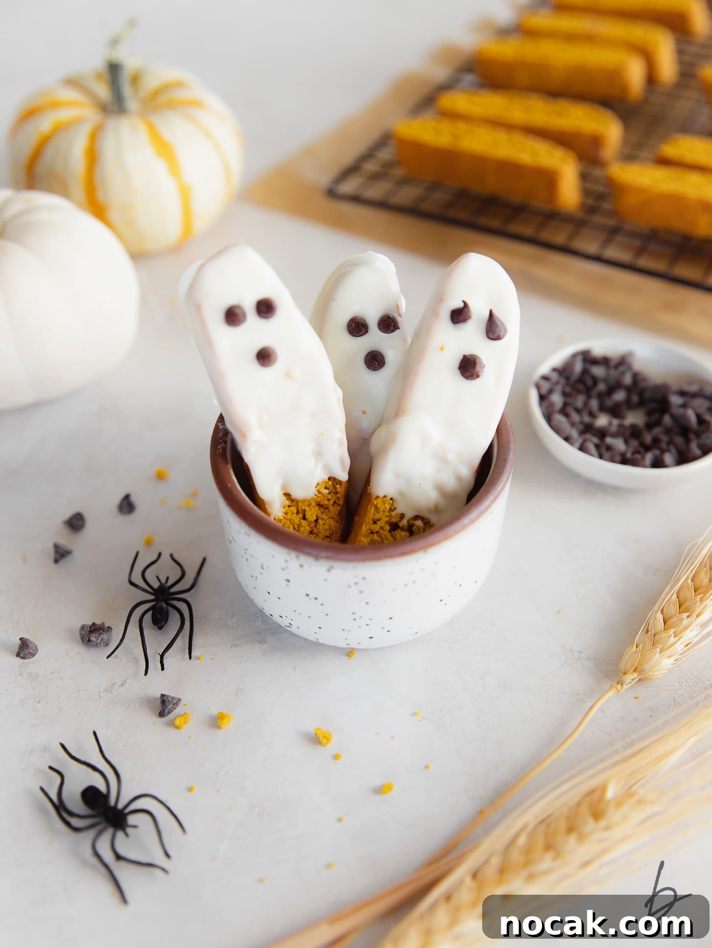 Pumpkin Spice Biscotti Recipe: Crunchy Autumn Cookie Guide 6 A cup with three white chocolate dipped pumpkin biscotti decorated to look like ghosts.