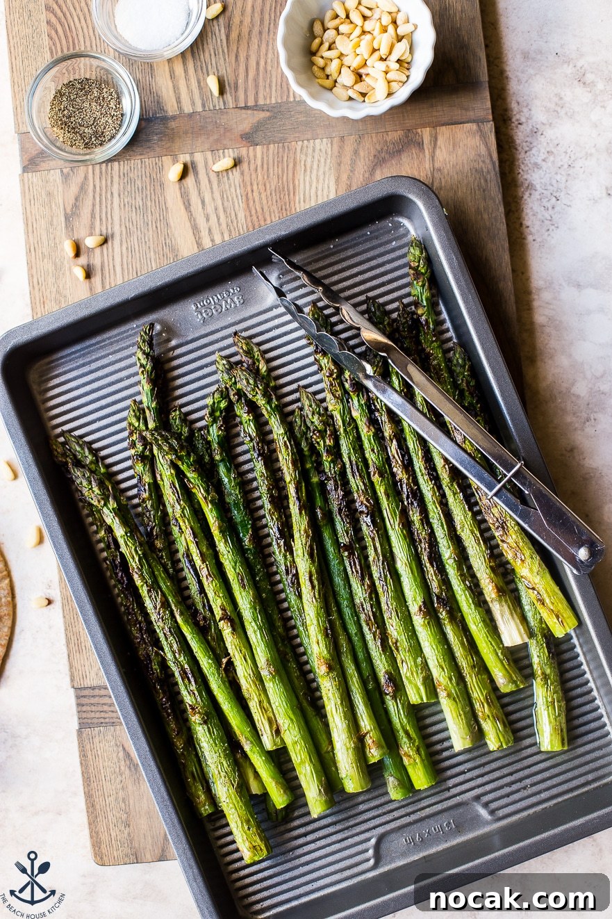 Overhead photo of grilled asparagus on a silver baking sheet with a pair of tongs