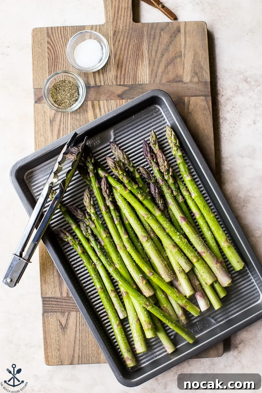 Pre-grilled asparagus on a silver baking sheet with a set of tongs