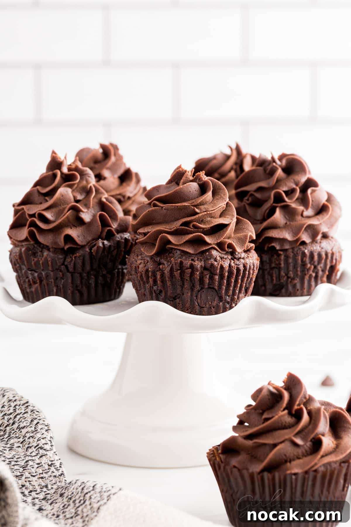 Fudgy Brownie Cupcakes with Gooey Chocolate Centers 14 Brownie Cupcakes on a serving platter, frosted, and one cupcake just under the platter.