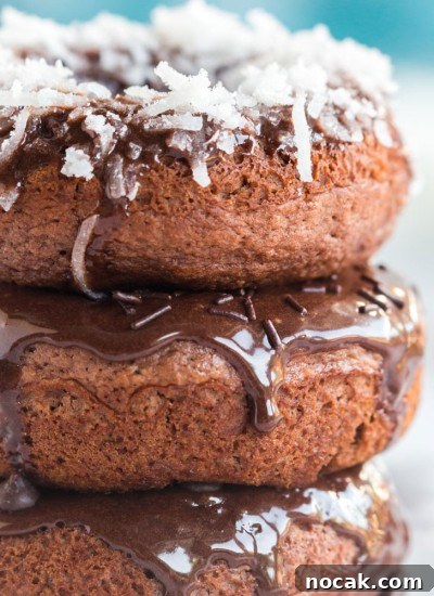 stack of chocolate baked donuts with chocolate frosting and toppings: coconut, sprinkles, and mini chocolate chips, on white plate