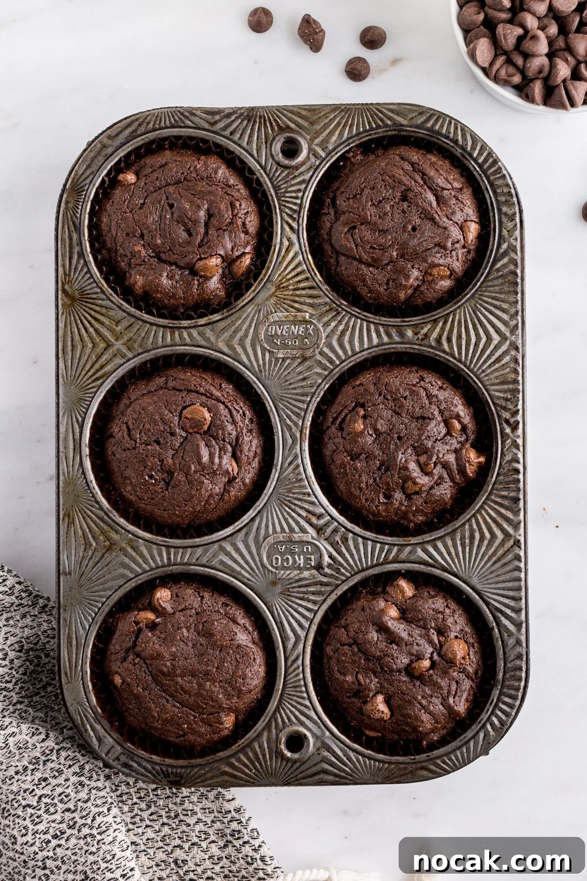 Fudgy Brownie Cupcakes with Gooey Chocolate Centers 9 Fully baked cupcakes in the cupcake tin on the counter, with a cloth under and chocolate chips off to the side.
