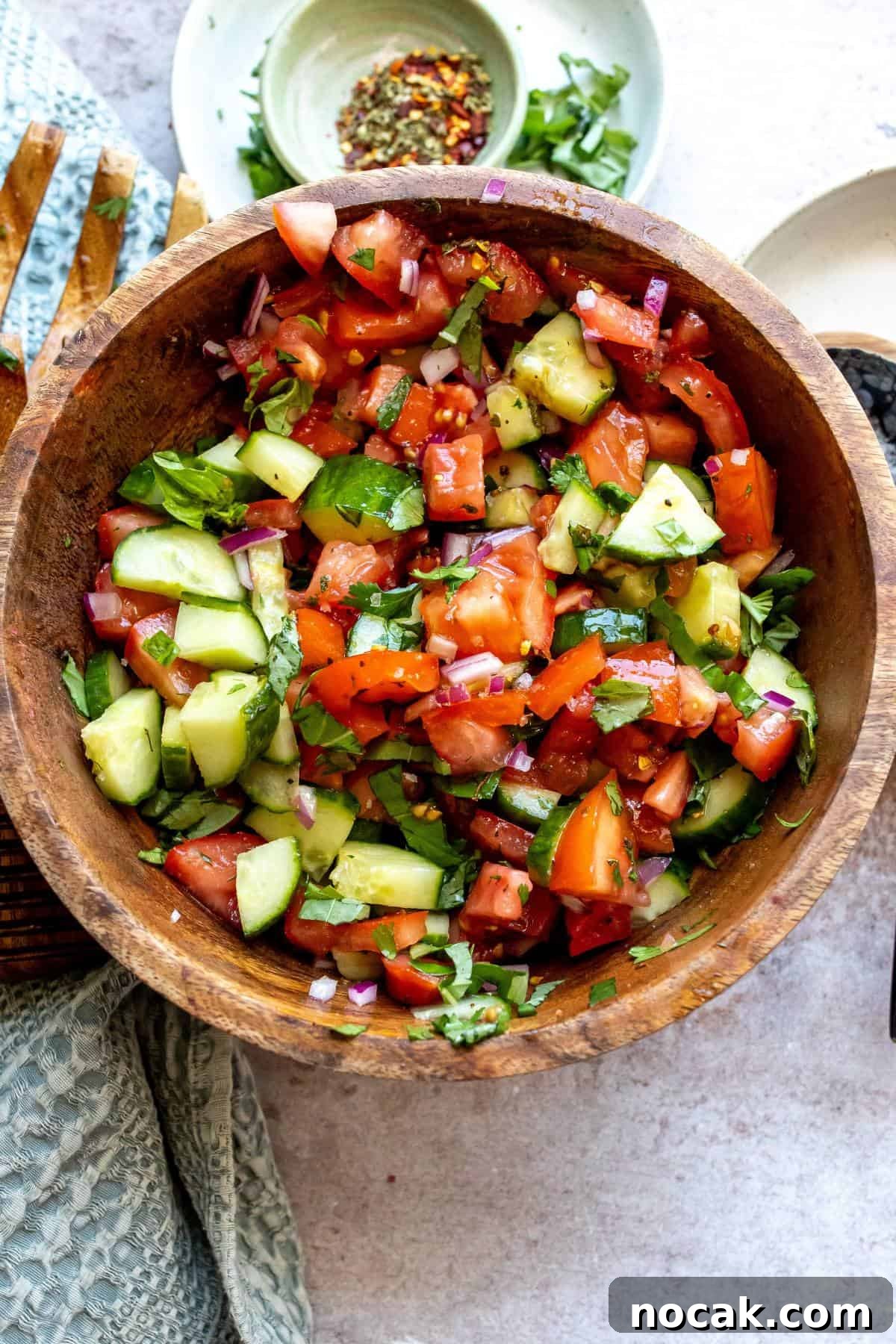 Cucumber and Tomato Salad with Fresh Herbs and Lemon Dressing 2 Wooden bowl with tomatoes and cucumber in it, red pepper flakes on the side.