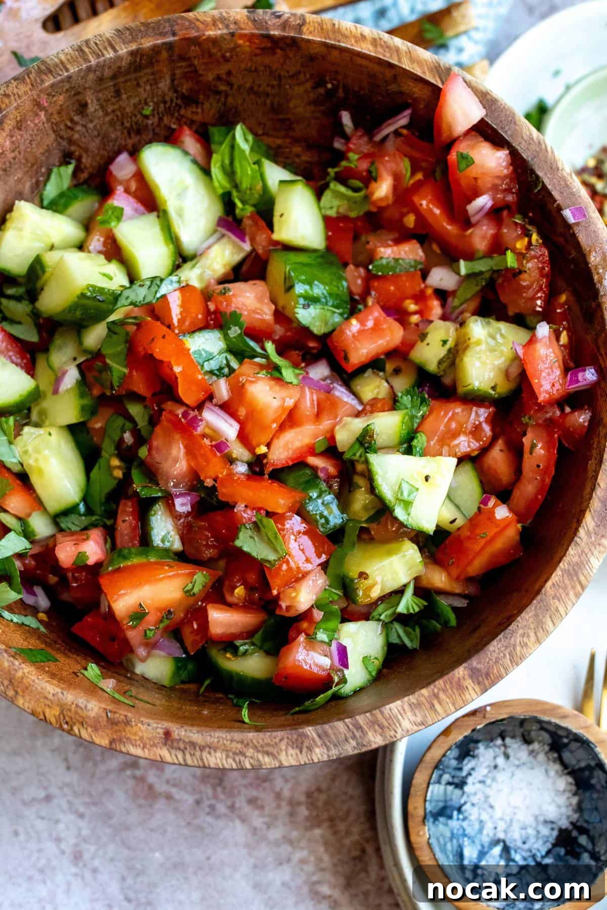 Cucumber and Tomato Salad with Fresh Herbs and Lemon Dressing 5 Wooden bowl with tomatoes and cucumber in it, red pepper flakes on the side.