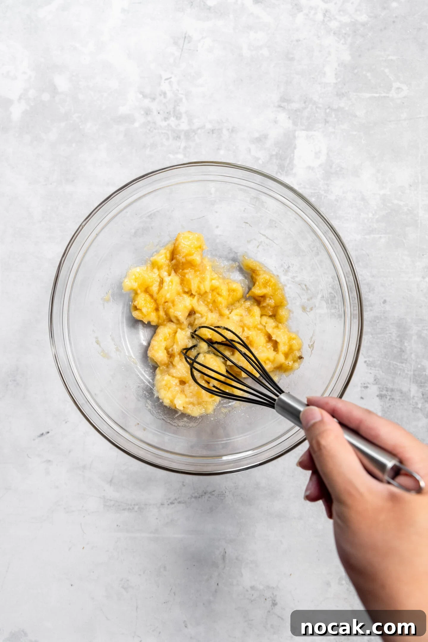 Bananas being mashed by a whisk in a mixing bowl