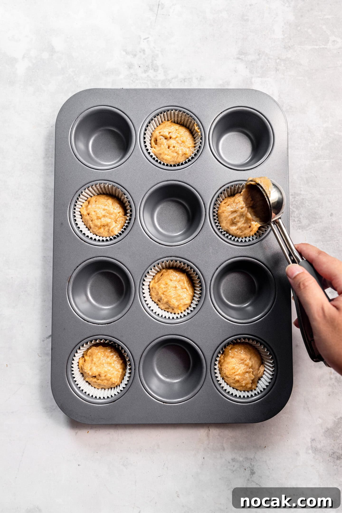 Muffin batter being scooped into a prepared muffin pan