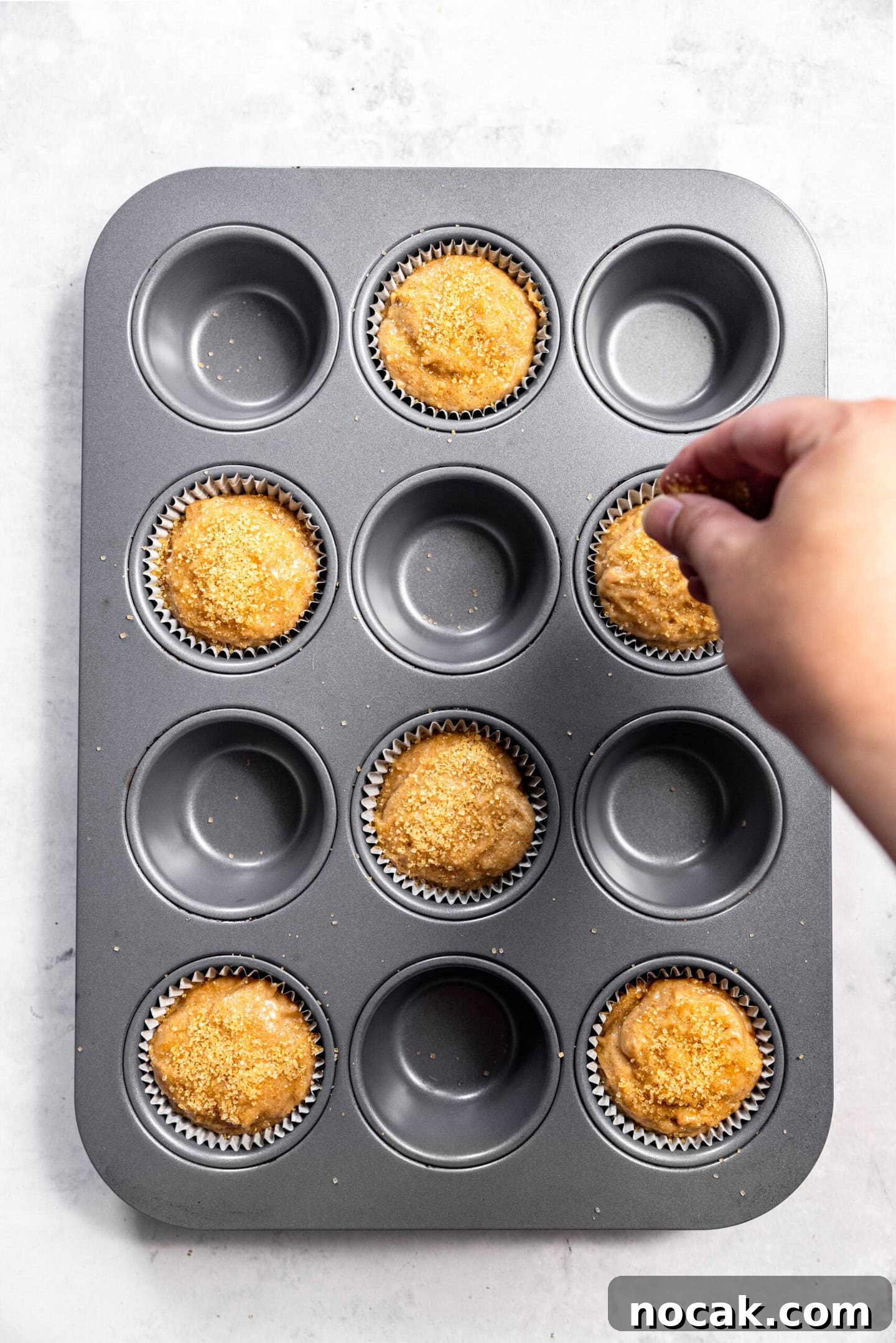 Turbinado sugar being sprinkled on top of muffin batter