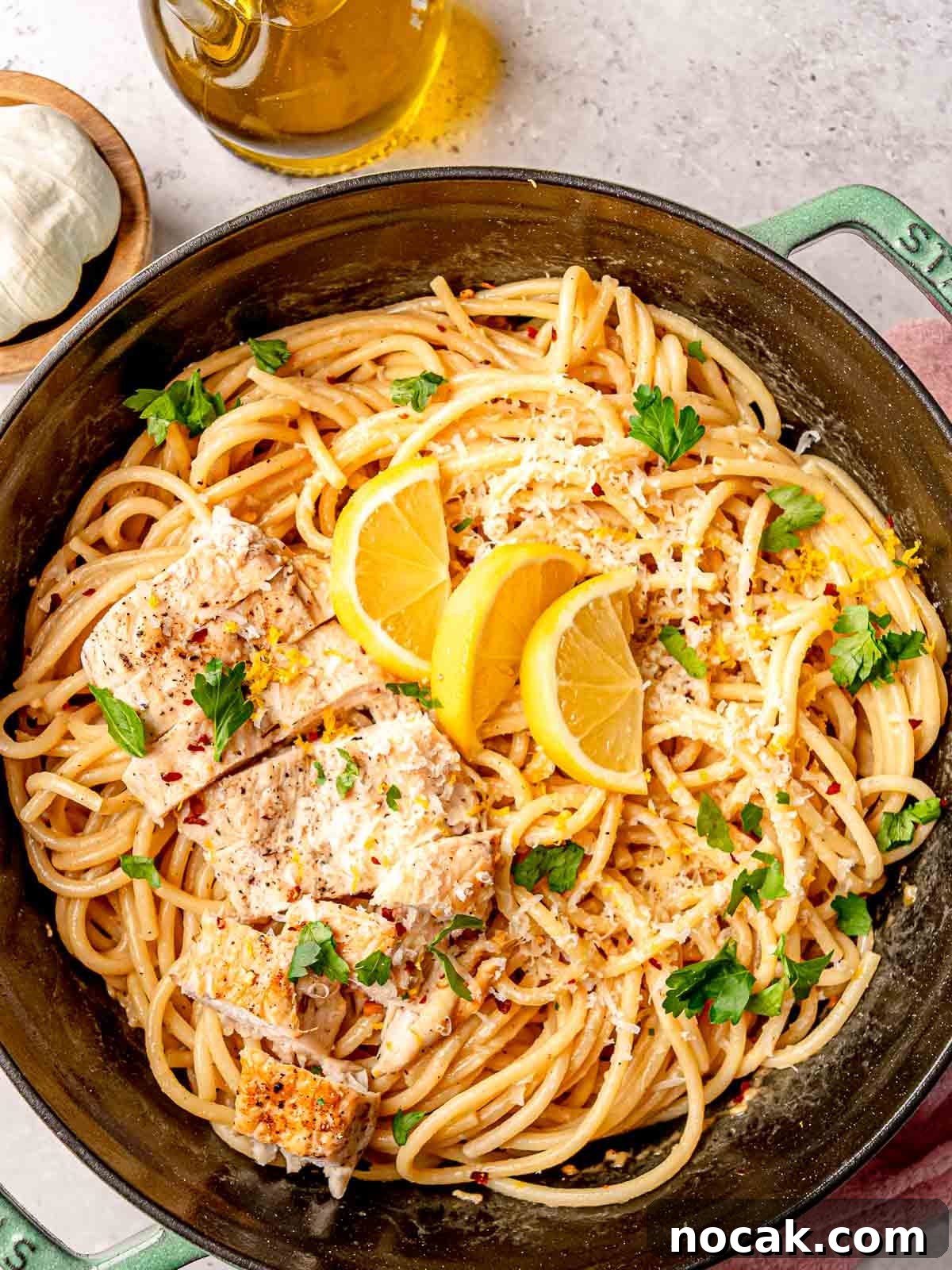 Lemon chicken pasta with lemon slices and fresh parsley, served in a green enameled cast-iron pan.