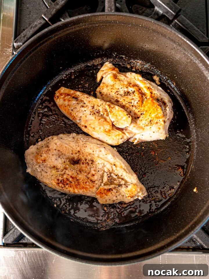 Two pieces of seasoned chicken breasts searing in a cast-iron pan, showcasing a golden-brown crust.