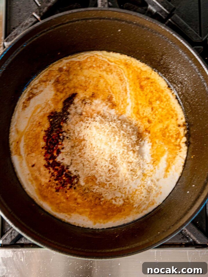 Creamy sauce with parmesan, heavy cream, and red pepper flakes simmering in a pan on the stove.
