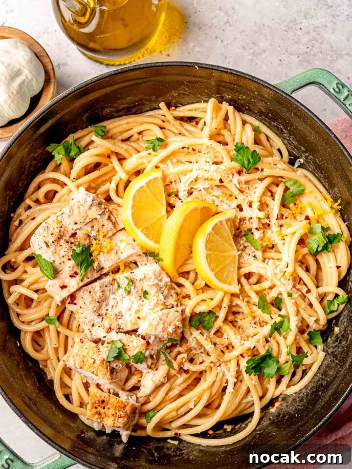 Lemon chicken pasta with lemon slices and fresh parsley, served in a green enameled cast-iron pan.