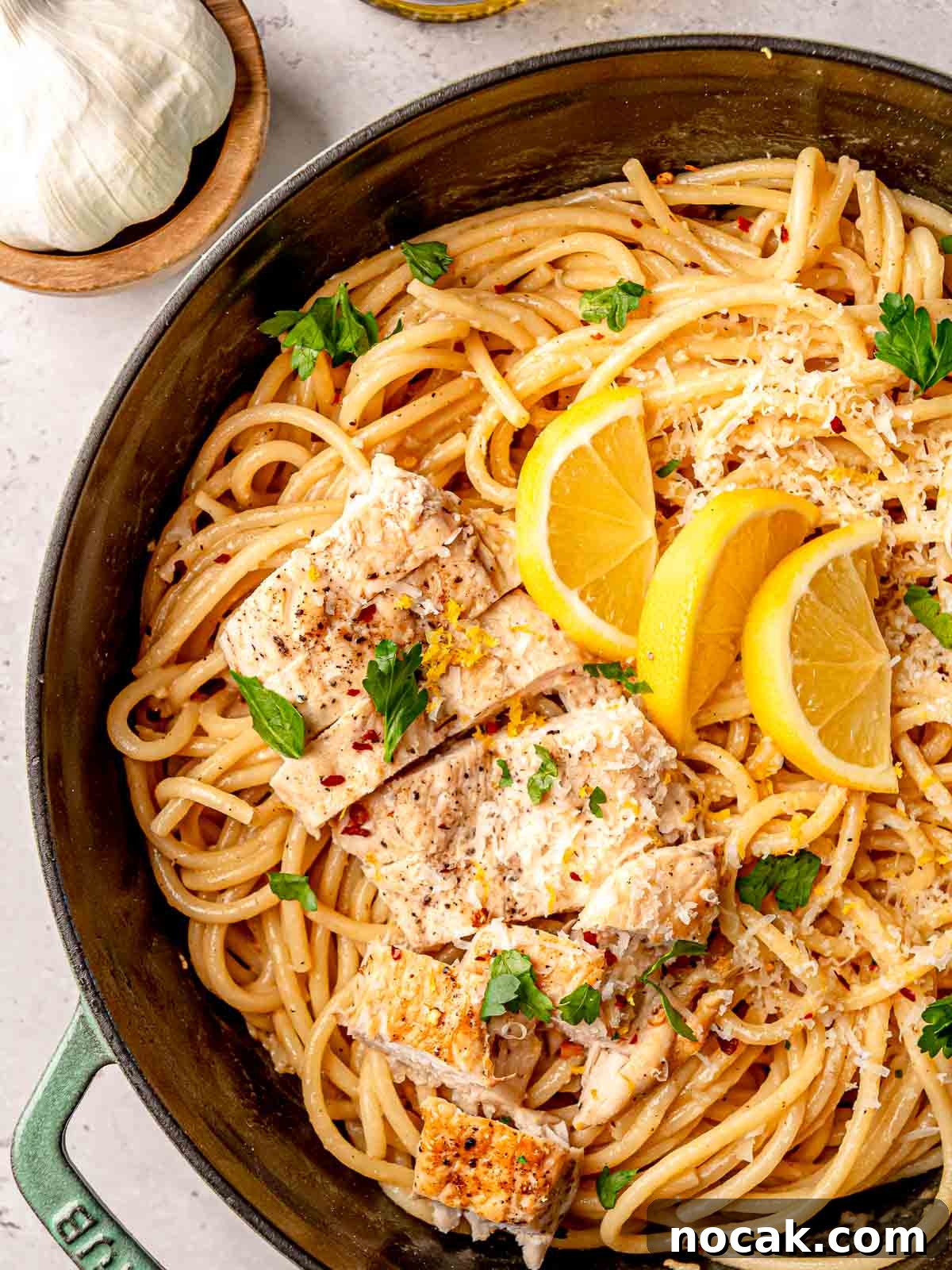 Creamy lemon chicken pasta, garnished with lemon slices and fresh parsley, served in a green enameled cast-iron pan.