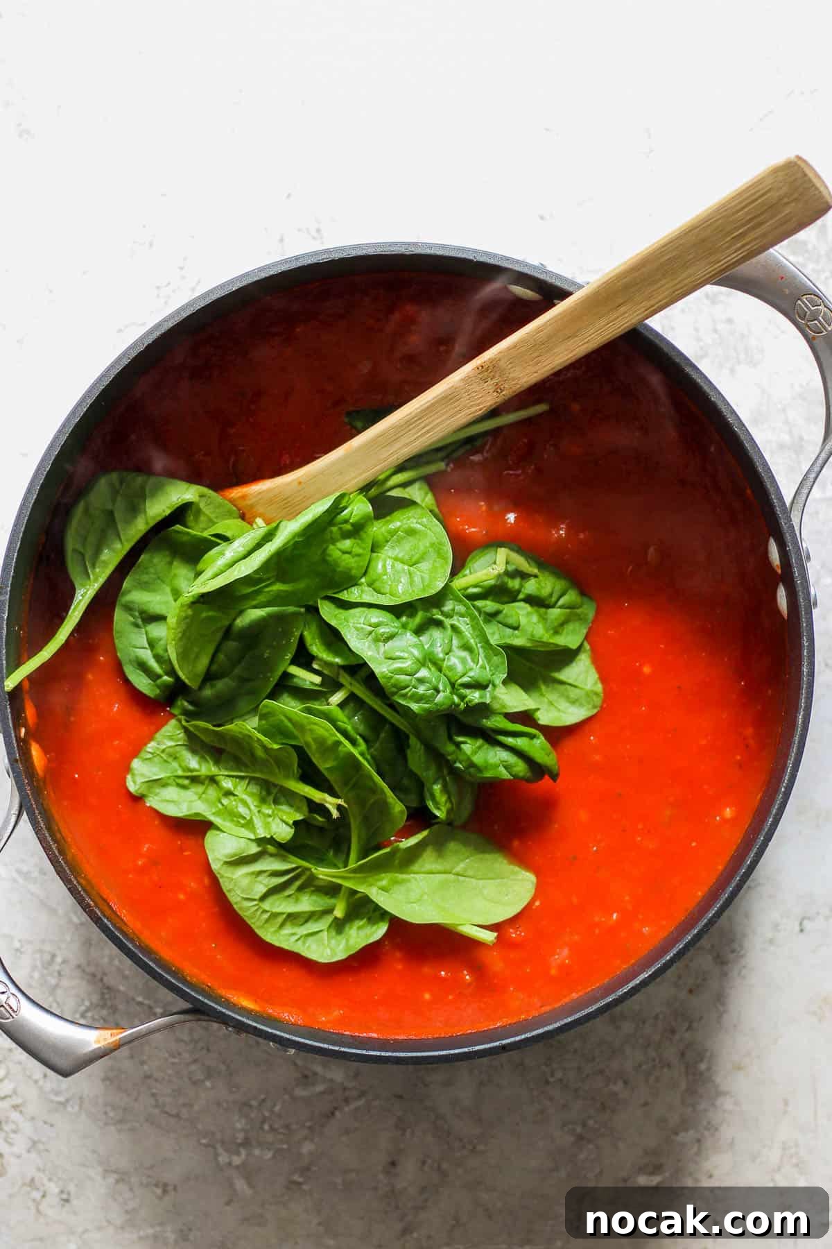 Spinach leaves toss in to the pot of soup and a wooden spoon.