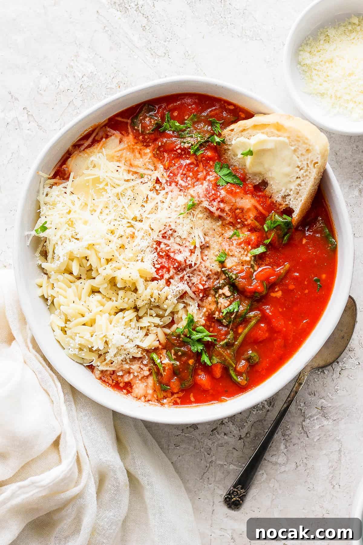 A fully topped bowl of tomato florentine soup with a small bowl of parmesan cheese on the side.