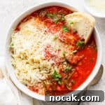 Top down shot of a bowl of tomato florentine soup with orzo, parmesan cheese and piece of sourdough bread sticking out.