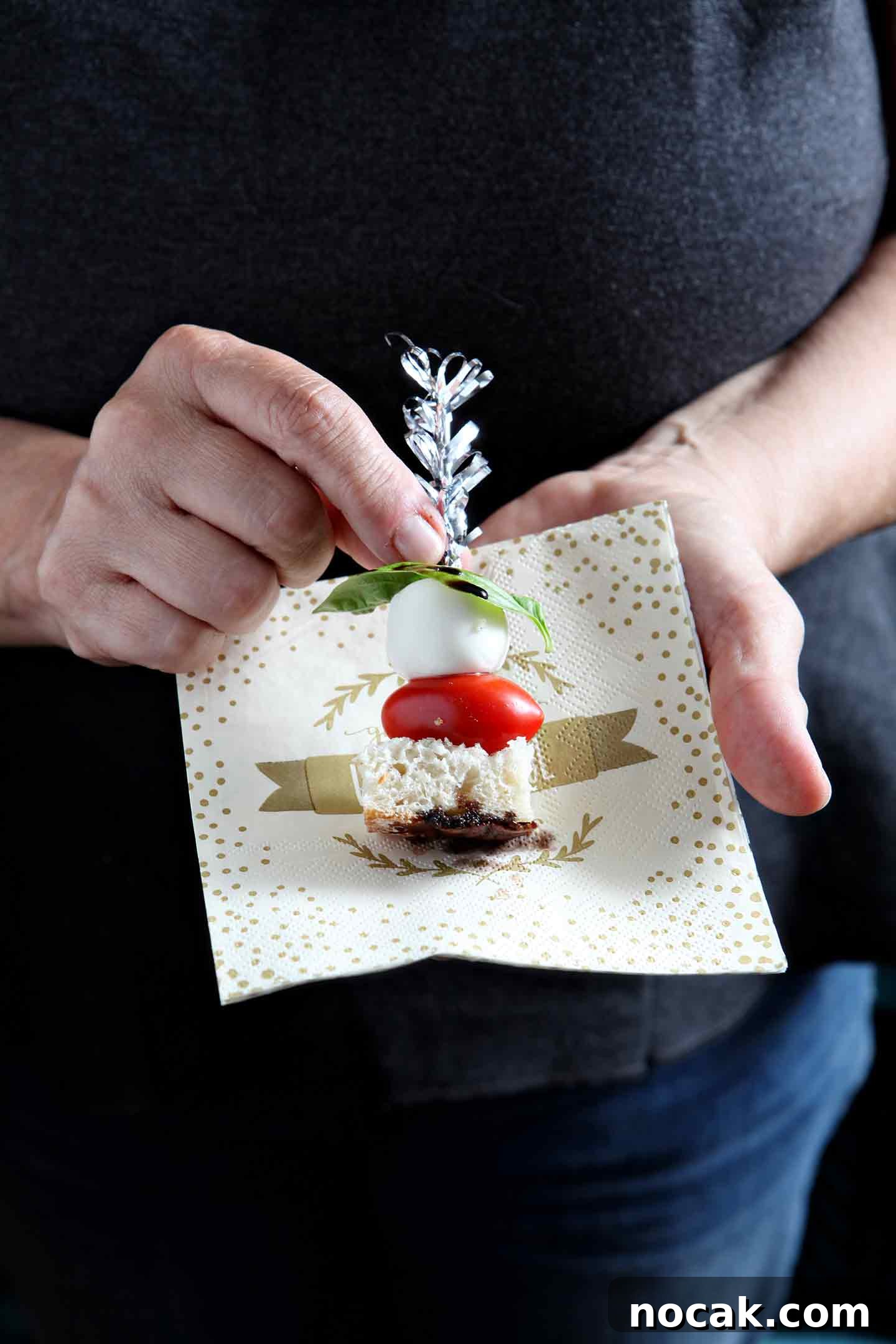 Caprese Skewers Recipe: Fresh Tomato, Mozzarella & Basil Bites 2 hand holding caprese skewers on a napkin