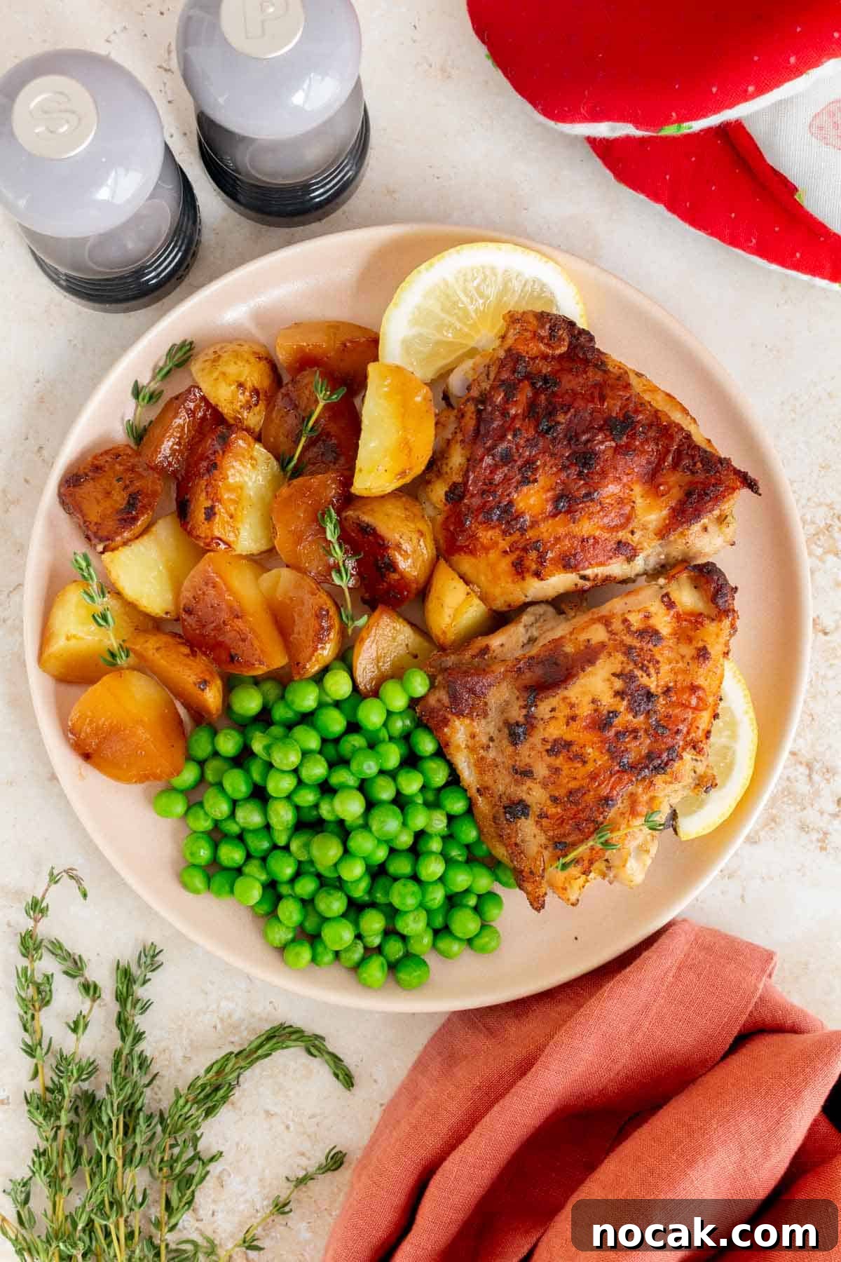 Crispy Cast-Iron Chicken Thighs with Roasted Potatoes 7 A plate with cast iron chicken thighs and potatoes along with peas and lemon slices.