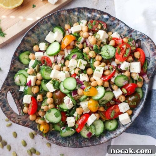 bowl with cucumber chickpea feta salad topped with various herbs and tossed in the dressing.