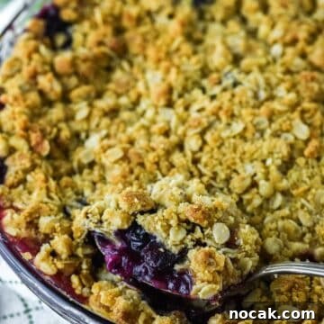 close-up of spoon lifting apple and blueberry crumble out of glass pie dish