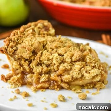 Slice of apple crumb pie on white plate.