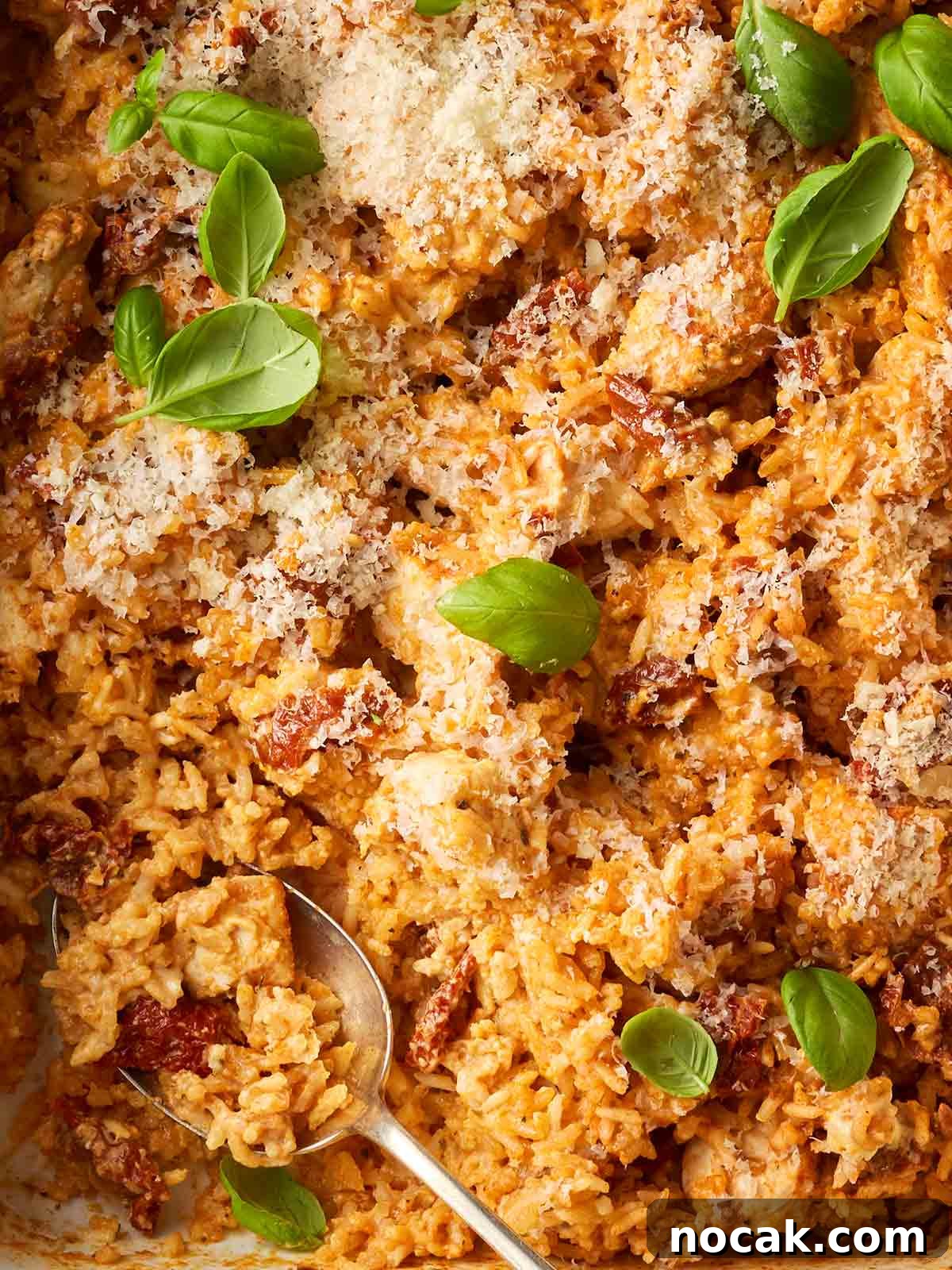 Marry Me Chicken and Rice — One-Pan Dump and Bake Recipe 3 A close up of a rice and chicken dish with sun-dried tomatoes and parmesan sprinkled on, garnished with basil leaves.