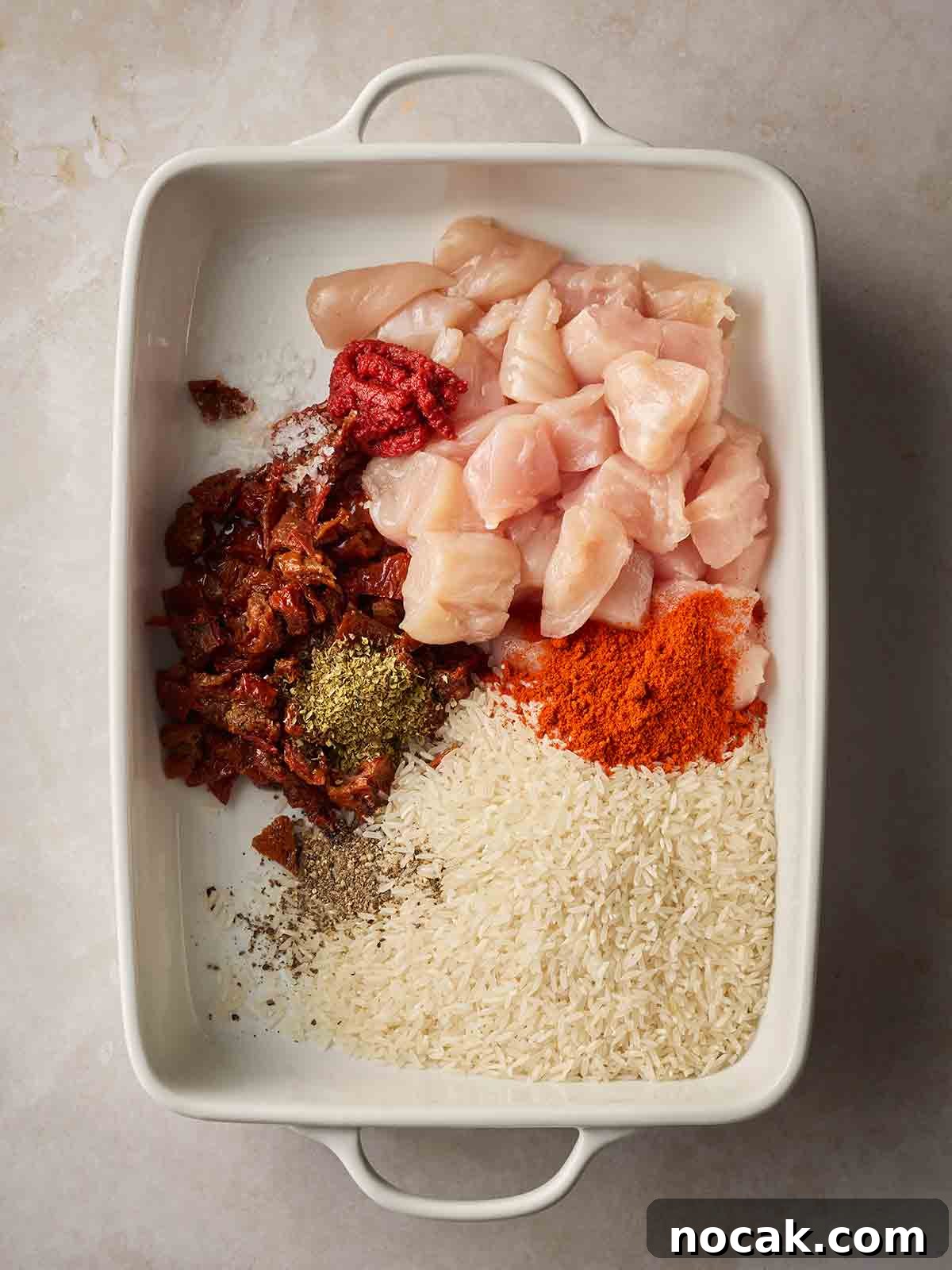 Marry Me Chicken and Rice — One-Pan Dump and Bake Recipe 5 Raw ingredients including chicken cubes, rice, sun-dried tomatoes and herbs, in an oven dish, ready to cook together in the oven.