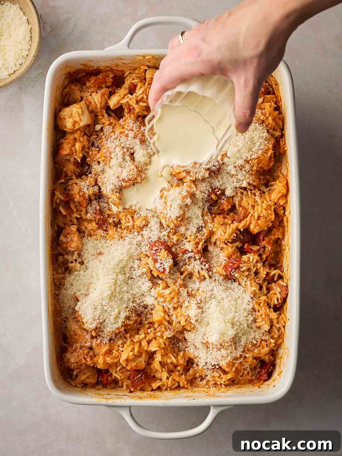 Marry Me Chicken and Rice — One-Pan Dump and Bake Recipe 8 A hand pouring cream into an oven dish of cooked chicken and rice.