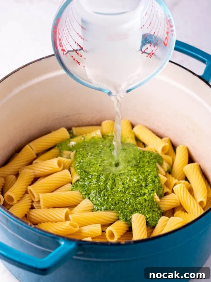 Pesto Rigatoni with Burst Cherry Tomatoes and Creamy Burrata 9 liquid measuring cup pouring starchy pasta water into a pot with cooked rigatoni and pesto