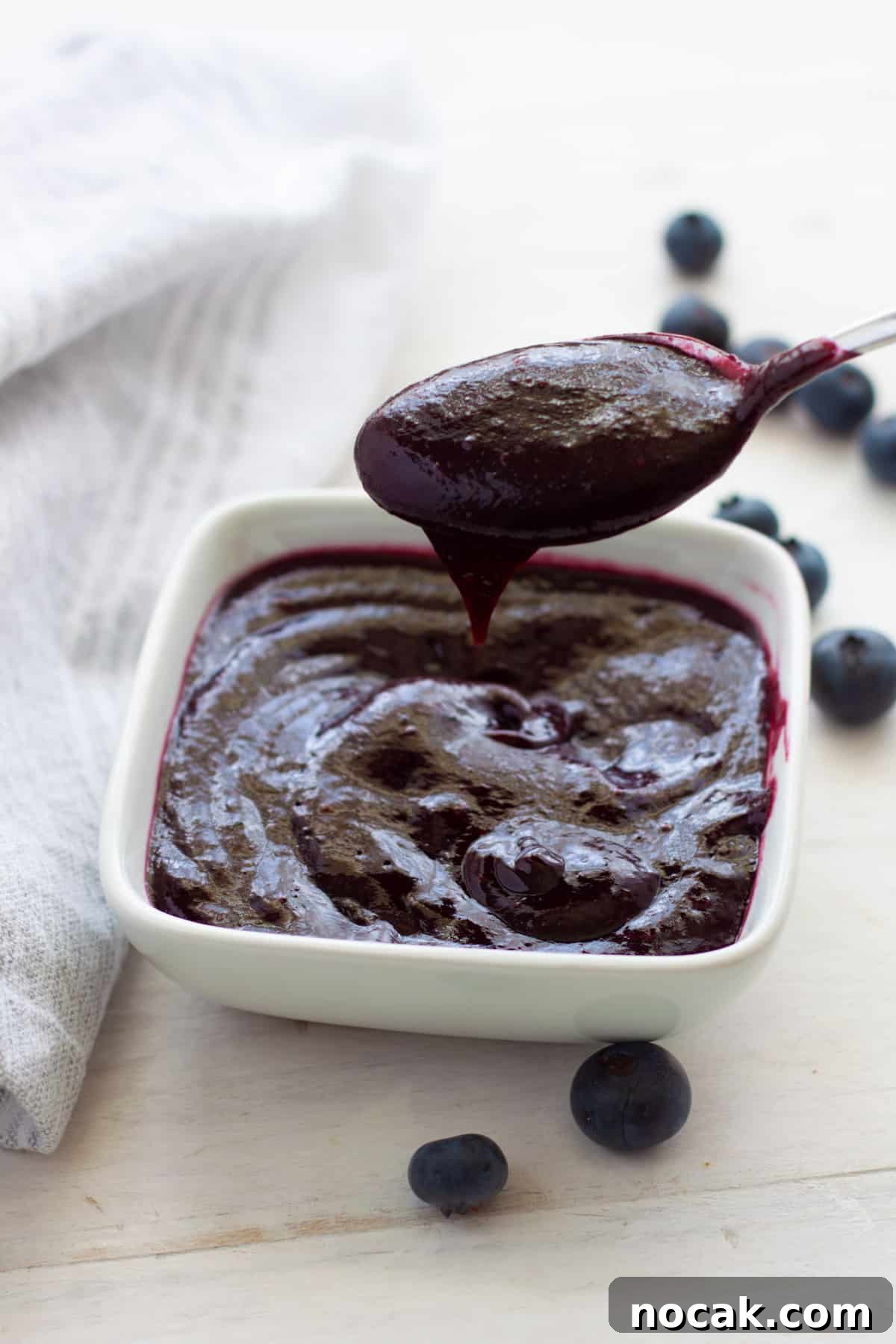 A spoon dipped into a small bowl of blueberry bbq sauce.