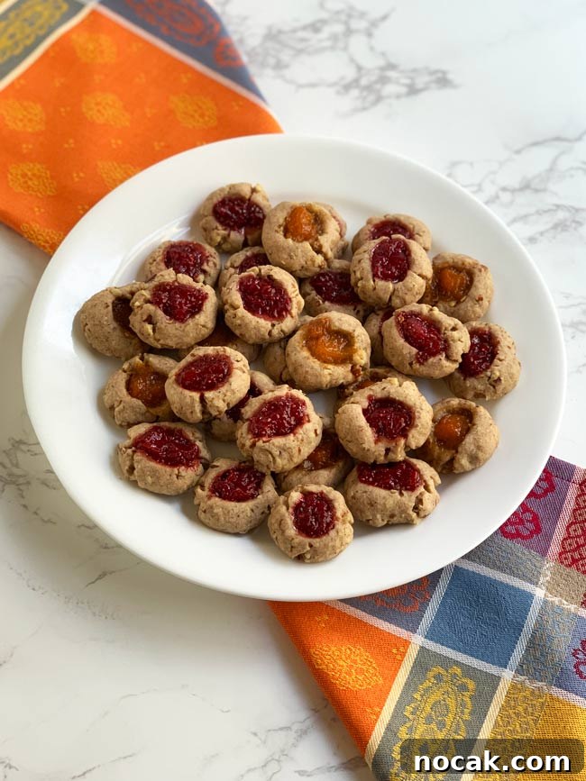 Jam Thumbprint Cookies: Baking Memories at a Cookie Party 2 Jam thumbprint cookies on white plate with multi-colored napkin.