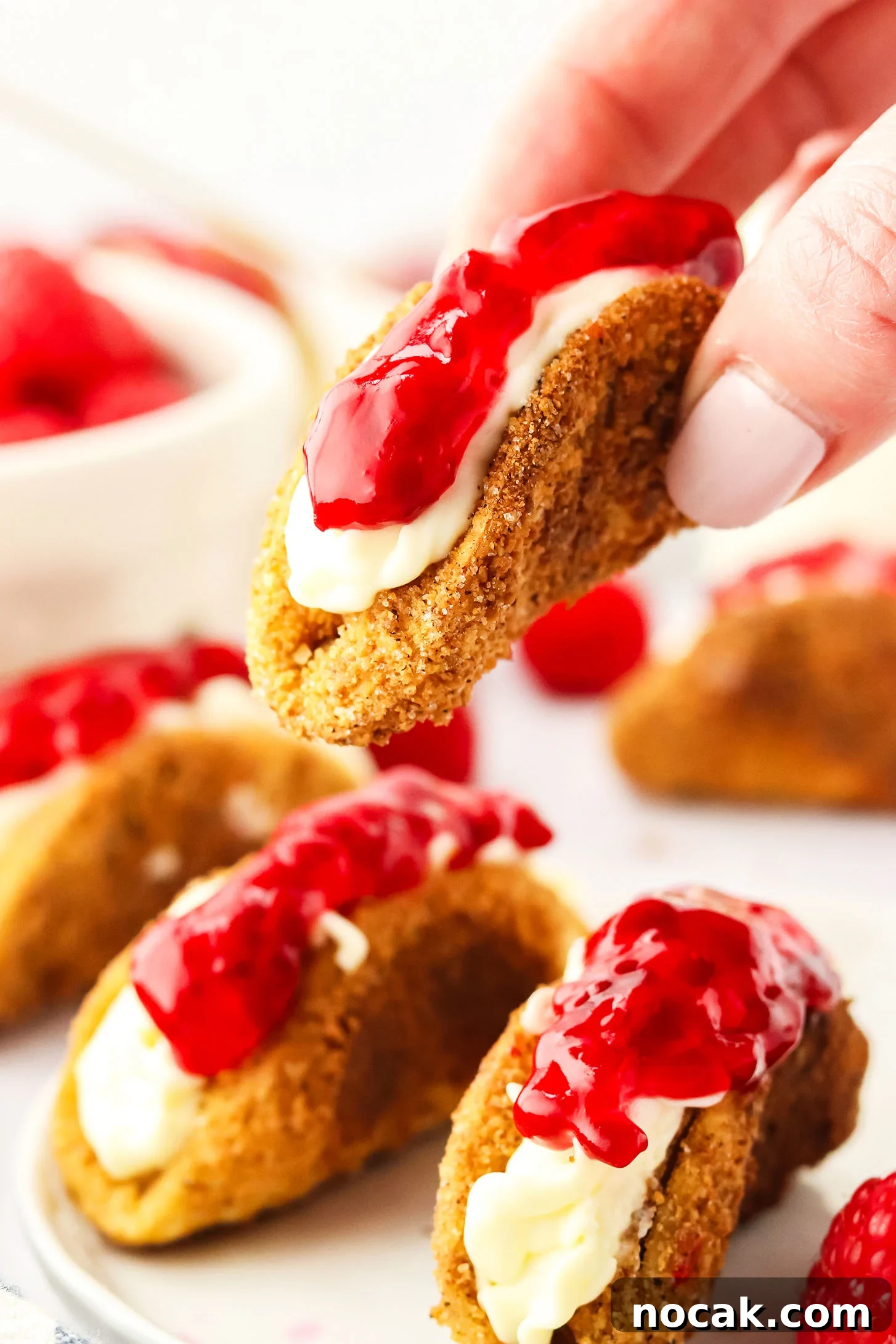 Raspberry Cheesecake Tacos: Creamy Dessert Taco Recipe 11 hand holding a cheesecake taco above a plate of cheesecake tacos