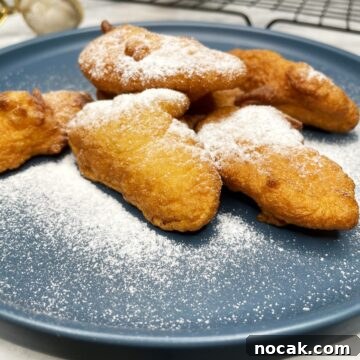 French apple fritters sprinkled with icing sugar on a blue dessert plate.
