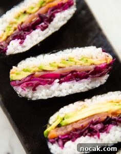 sushi sandwich close up shot of 3 salmon sushi sandwiches on black serving plate