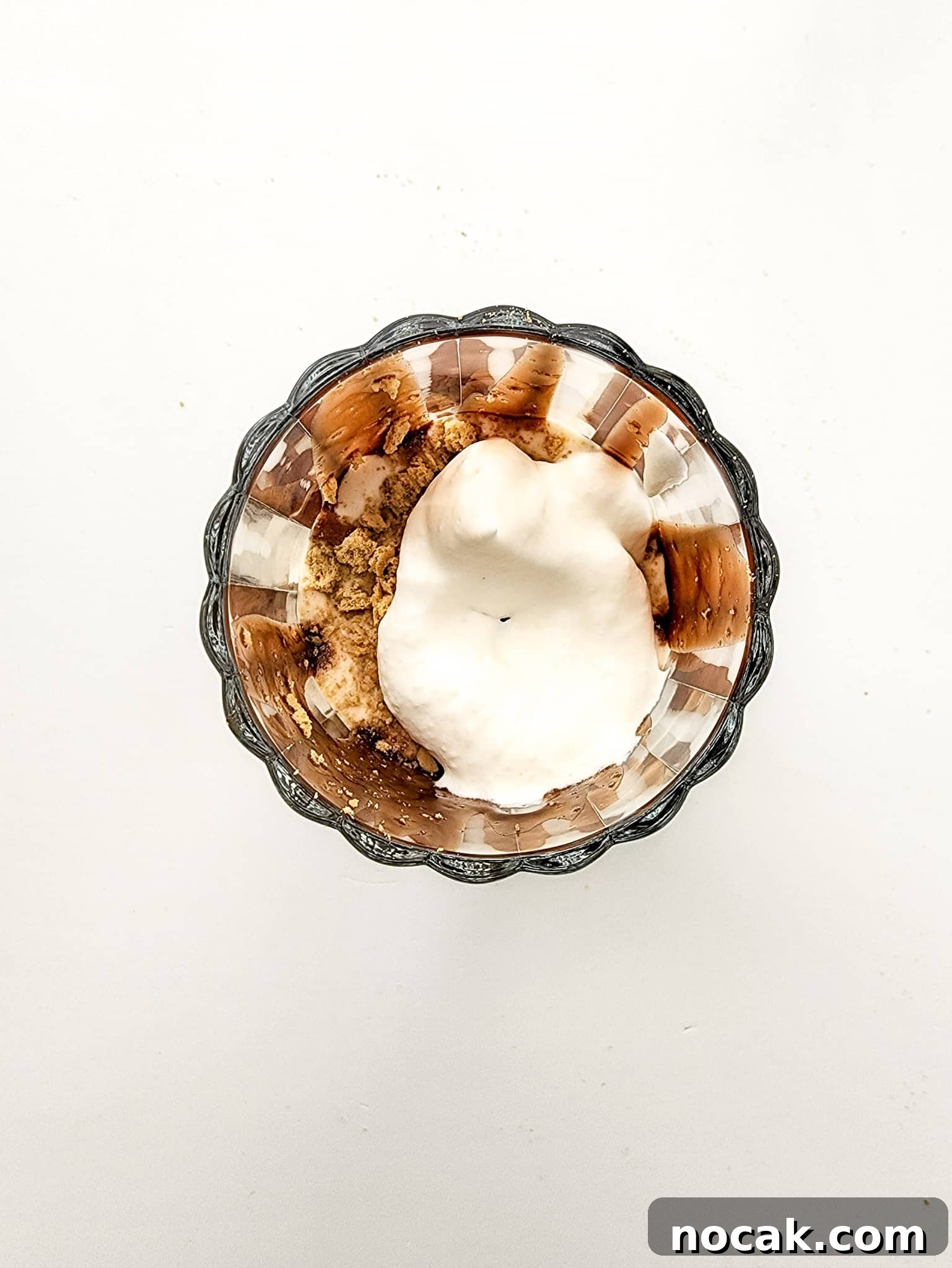 DIY S'mores Frappuccino: Starbucks Copycat Recipe for Home 6 Image of glass cup filled with crushed graham crackers and whipped cream over a white background.