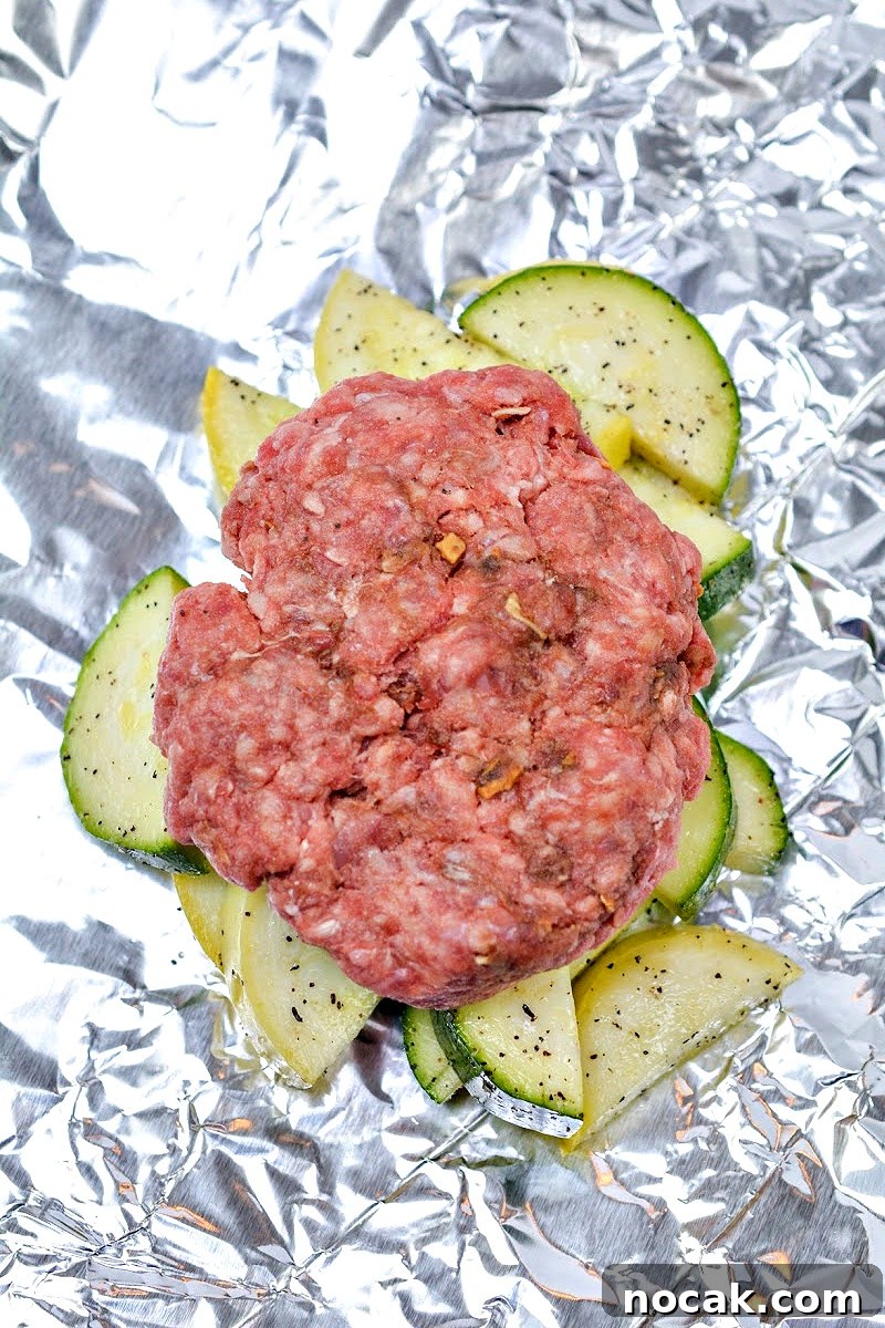 Keto Cheeseburger Foil Packets for Air Fryer Cooking 11 Raw burger on top of veggies in a foil packet