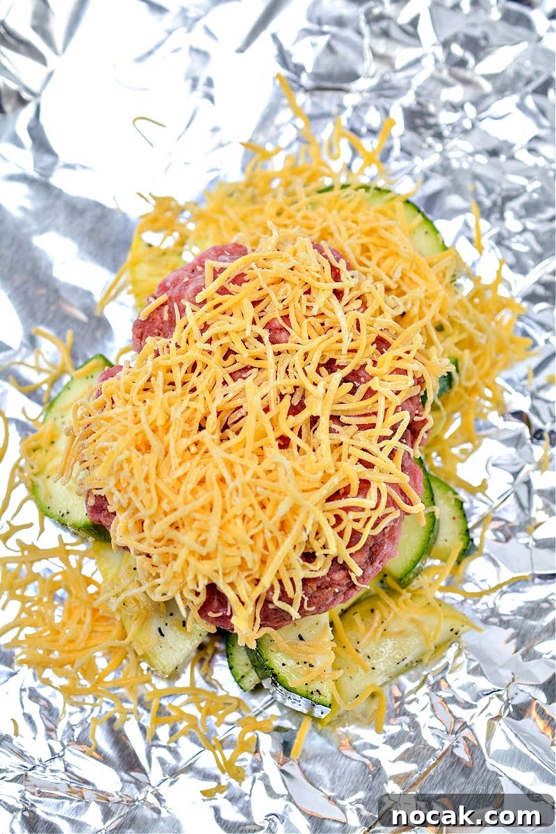 Keto Cheeseburger Foil Packets for Air Fryer Cooking 12 Shredded cheese on top of raw burger and veggies in a foil packet