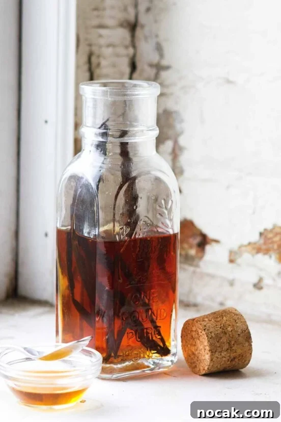A bottle half-filled with vanilla syrup and a couple vanilla beans inside. A cork rests beside the bottle.