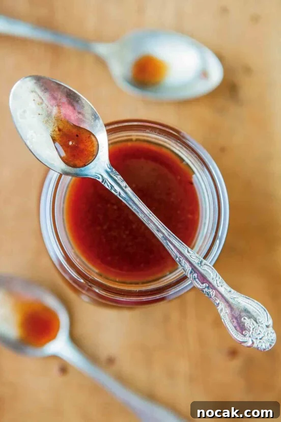 A jar of pumpkin spice syrup with a spoon resting on top and two spoons beside the jar.