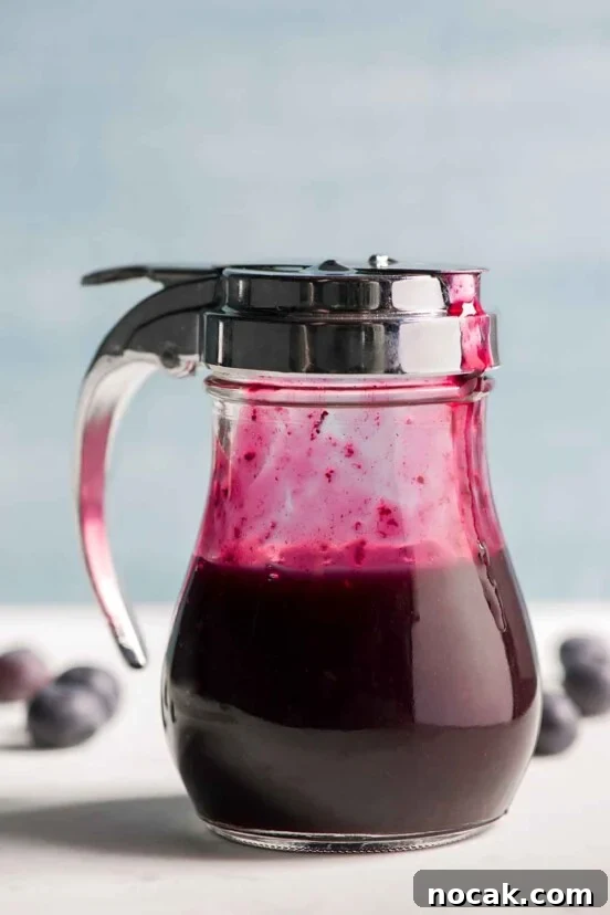 A diner-style dispenser half-filled with blueberry syrup.