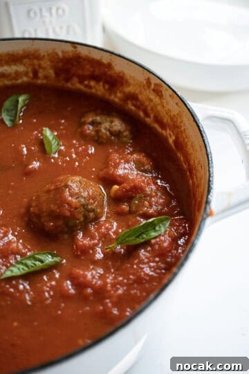 Classic Italian Fried Meatballs Recipe — Crispy, Savory Plates 11 A pot filled with sauce and meatballs, garnished with basil.