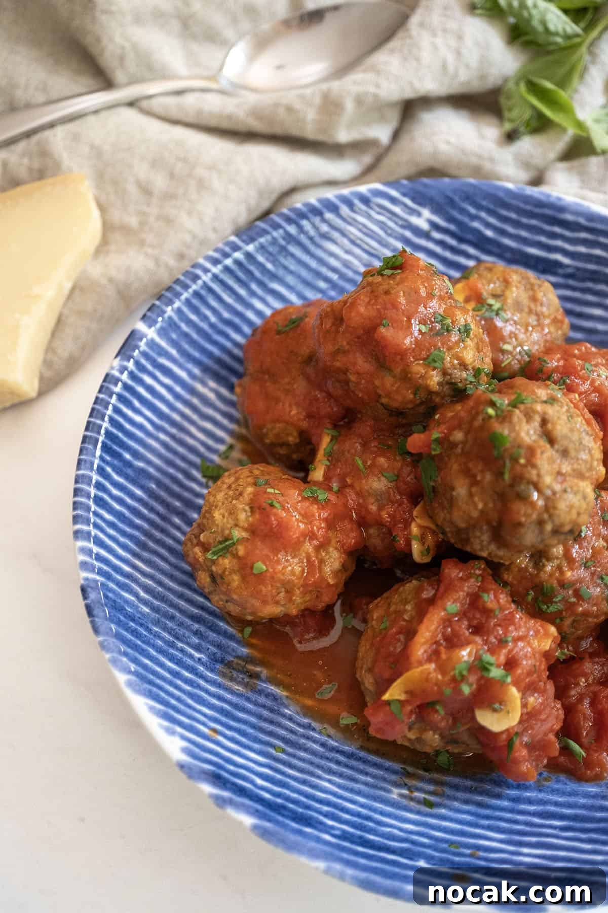 Classic Italian Fried Meatballs Recipe — Crispy, Savory Plates 12 Meatballs covered in tomato sauce in a bowl with a block of parmesan cheese on the side.